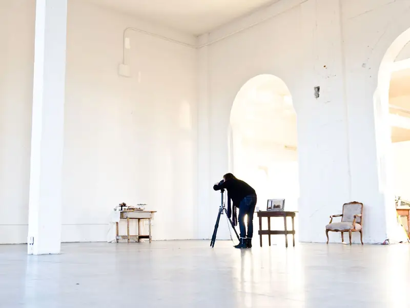 En fotograf med et kamera på stativ i et lyst, hvidt studie