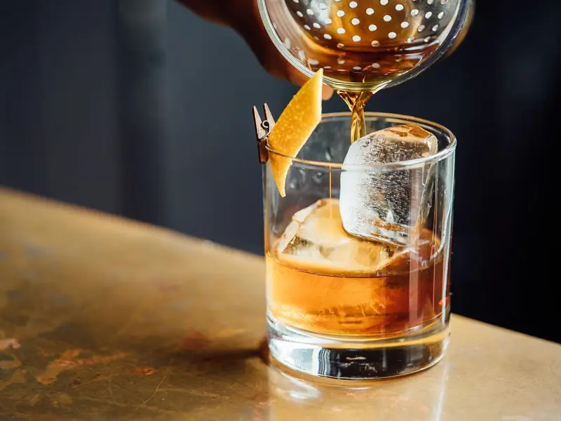 A cocktail being strained over ice into a glass with orange peel