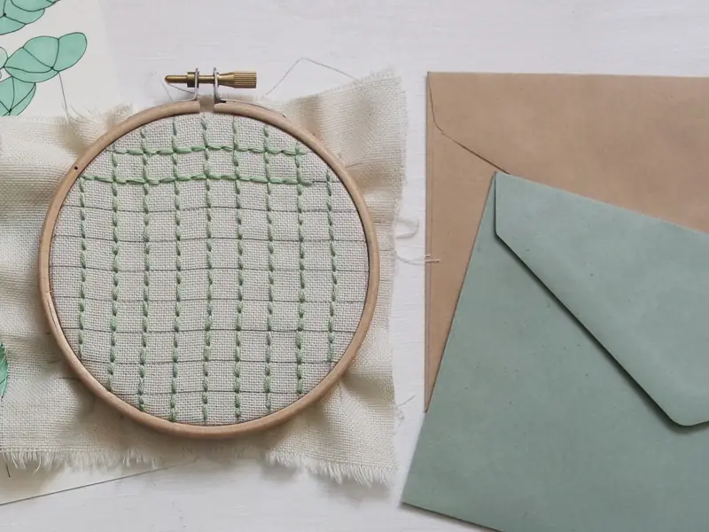 En broderiramme med grønt broderi i gang på hør