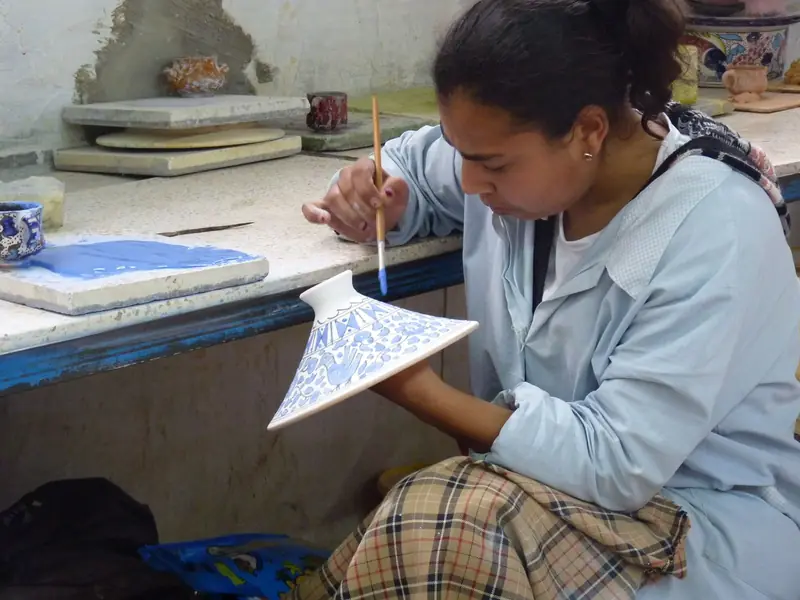 A woman painting a design onto a ceramic piece