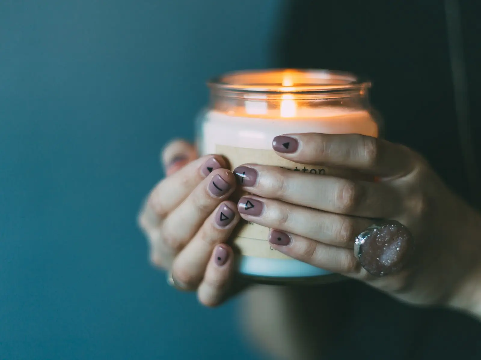 Hands holding a lit candle in a glass jar