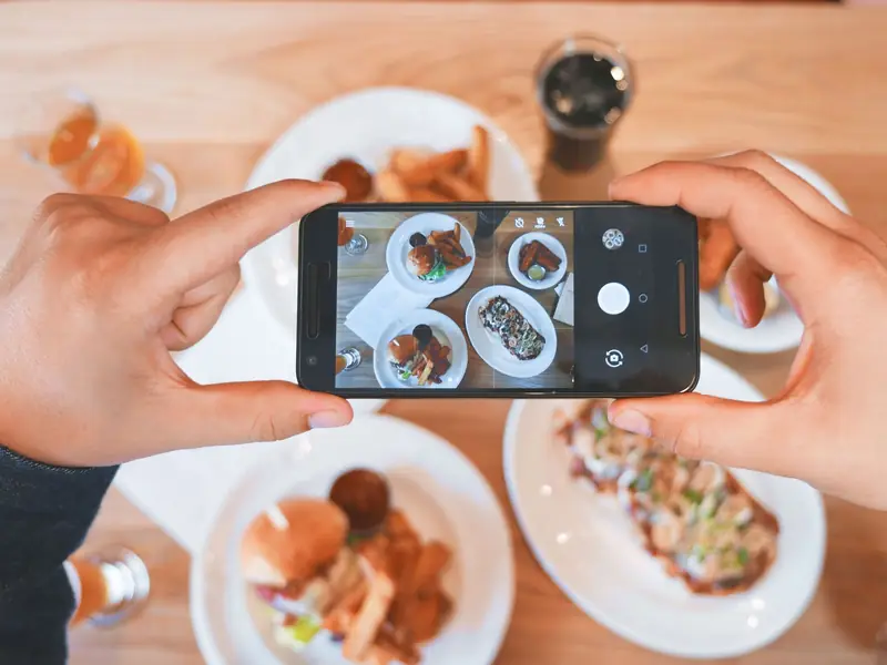 Hände fotografieren mit dem Handy einen Tisch voller Essen