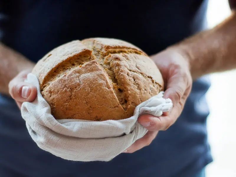 Hands holding a fresh loaf of bread in a cloth