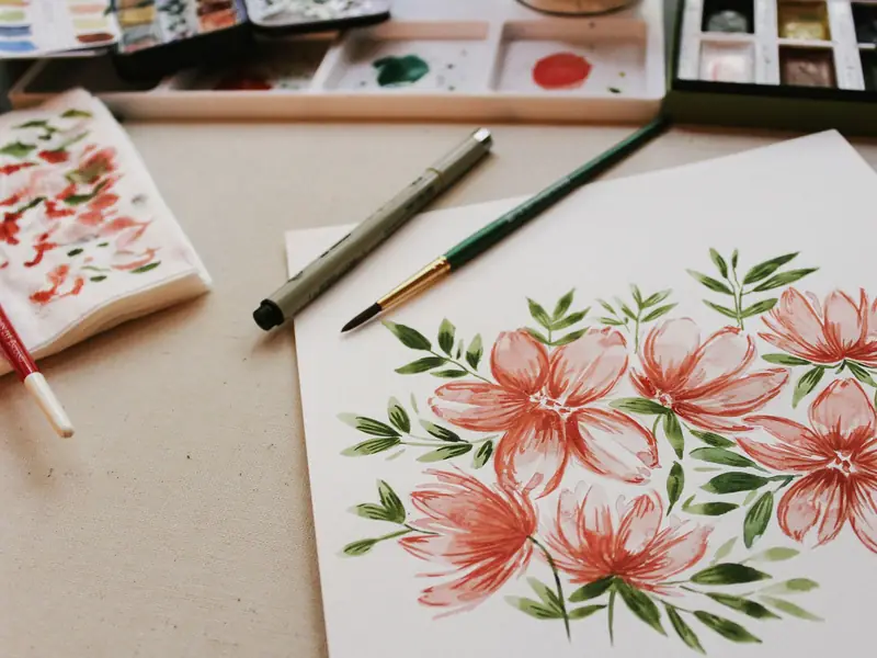 A watercolour painting of flowers beside a paint palette and brushes